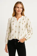 Blusa color crema con estampado de hojas color marrón, cuello mao con abertura y botones, mangas largas abullonadas con puños elásticos.