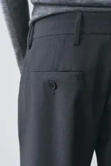 Pantalón de vestir gris oscuro de tiro bajo, con trabillas en la cintura, bolsillos delanteros y traseros, raya planchada y pierna recta.