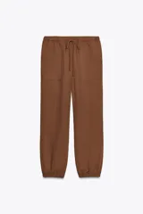 Pantalón jogger marrón de tiro alto con cintura elástica ajustable con cordones, bolsillos delanteros y traseros de parche con solapa. Bajo con puño elástico.