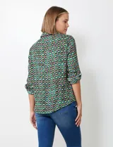Blusa de gasa con estampado geométrico en tonos verdes, azules y morados. Presenta cuello con solapa, escote en V con botones y mangas largas que se pueden remangar y sujetar con presilla.