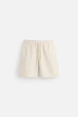 Bermuda color crema de algodón con cintura elástica ajustable con cordón, corte regular, bolsillos laterales y trasero de vivo.