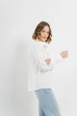 Camisa blanca de voile con bordados calados en el frente, cuello camisero, mangas largas con puños abotonados y cierre frontal con botones. 