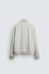 Cazadora color gris claro de corte regular, confeccionada en tejido con efecto ante. Tiene cuello alto, cierre frontal con cremallera, bolsillos laterales y puños y bajo en rib elástico.
