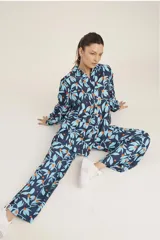 Conjunto de camisa de manga larga con botones y pantalón de corte recto, ambos con estampado de hojas y flores en tonos azul y naranja sobre fondo azul marino.