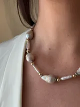 Collar corto de perlas de río alargadas y ovaladas, con cuentas de acero quirúrgico y bolitas con baño de oro. Cierre con cadena de acero quirúrgico y gancho para regular el largo.