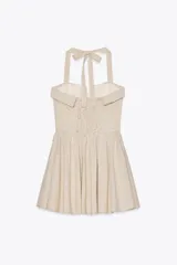 Vestido corto a cuadros beige y blanco, con cuello halter que se ata en la nuca, escote recto con abertura y falda acampanada. Tiene bolsillos laterales ocultos, espalda elastizada y botones decorativos en el frente.