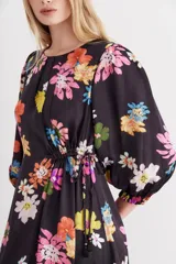 Vestido midi negro con estampado de flores grandes y coloridas (rosado, naranja, amarillo, blanco, azul). Presenta mangas balloon, escote redondo con tablas y ajuste en la cintura con lazo.