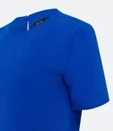 Blusa blanca de poliéster con cuello redondo, mangas cortas, cierre trasero en forma de gota, pequeñas aberturas laterales y acabados en pespuntes en las mangas y el cuello.