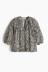 Blusa de popelina de algodón con estampado de hojas en blanco y negro. Tiene cuello mao, abertura en V con botones y mangas globo tres cuartos con puños finos.