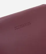 Neceser de poliuretano color borgoña, con forma trapezoidal y cierre de cremallera.