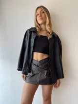 Sobrecamisa negra de ecocuero con cuello clásico, cierre frontal con botones a presión, mangas largas con puños abotonados, bolsillos de parche en el pecho y corte oversize.