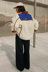 Campera color crema de corderito con cuello y ribetes en color marrón y detalles en azul.