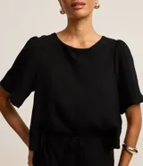 Blusa negra de mangas cortas abullonadas, confeccionada en tejido airflow con textura arrugada y abertura en forma de gota en la espalda.