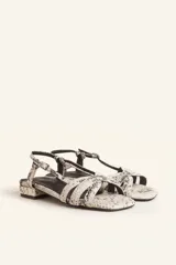 Sandalia baja de cuero charol negro con tiras entrecruzadas y pulsera al tobillo con hebilla.