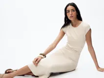 Vestido midi color beige confeccionado en hilatura con algodón. Tiene cuello redondo, manga corta caída y detalle de drapeado lateral.