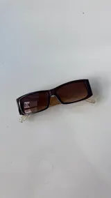 Lentes de sol rectangulares con armazón de acetato color marrón oscuro y lentes degradados en tonos marrones. Las patillas son transparentes con un detalle grabado en el extremo.