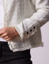 Chaqueta cruda de tejido boucle con flecos en el borde y botones negros en los puños.