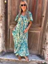 Vestido largo de seda, fluido y amplio, con mangas cortas y bolsillos laterales. Presenta un estampado en tonos turquesa y beige/crema.