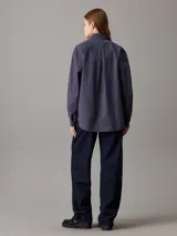 Camisa azul marino de popelín de algodón, corte holgado, cuello en punta, manga larga con puños abotonados, bolsillo de parche en el pecho e insignia con el monograma de Calvin Klein en el bolsillo del pecho.