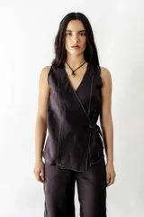 Blusa negra cruzada con lazo lateral, sin mangas y costuras blancas en contraste.