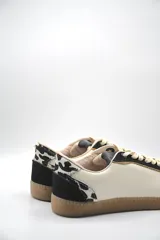 Zapatillas urbanas de cuero color beige con puntera y cordones marrones. Presentan un panel de animal print en el talón y suela de goma color caramelo.