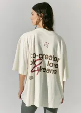 Remerón de jersey de algodón color crudo, de manga corta, con estampa en serigrafía en frente y espalda con la frase "co-creator of love & dreams" y un arco y flecha.