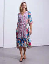 Vestido midi con estampado floral en tonos azules, rojos y blancos. Tiene escote en V, mangas 3/4 con puños fruncidos, cintura elastizada con lazo de ajuste y falda con volantes.