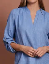 Blusa celeste con escote en V y mangas 3/4 regulables con presilla y botón.