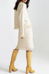 Conjunto tejido color crema, compuesto por un sweater de mangas largas con diseño trenzado y falda midi con diseño trenzado y flecos en el ruedo.