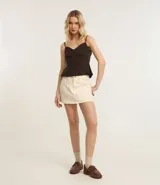 Short pollera corto de sarga color beige claro, con talle alto, trabillas en la cintura, bolsillos delanteros y cierre frontal.