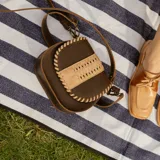 Bandolera de cuero color marrón con correa larga regulable, solapa con diseño trenzado y cierre con broche imantado.