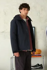 Campera con capucha de color azul marino, con cierre frontal impermeable y bolsillos laterales con cremallera. Presenta puños ajustables con velcro y un diseño técnico y minimalista.