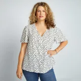 Blusa vaporosa con estampado de lunares, color blanco y negro, de manga corta y escote en V.
