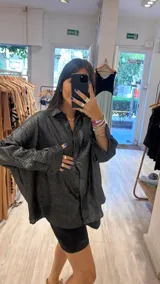 Camisa color beige claro con textura brillante, cuello clásico, cierre frontal con botones y mangas largas con puños abotonados.