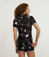Conjunto de pijama de dos piezas confeccionado en viscolycra, compuesto por una blusa de manga corta con cuello solapa y botones frontales, y un short con cintura elástica y lazo. Estampado integral de temática espacial con estrellas, planetas y explosiones en tonos rosados y blancos sobre fondo negro.