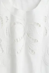 Remera blanca de algodón con cuello redondo y mangas cortas. Presenta un diseño calado en el frente.