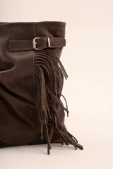 Botas de caña media color marrón chocolate, confeccionadas en cuero. Presentan un diseño arrugado en el empeine, una correa con hebilla metálica y flecos laterales.