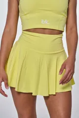 Conjunto deportivo amarillo compuesto por un top con logo "bk." y una minifalda tableada.