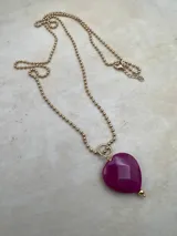 Collar dorado con cadena de bolitas y dije de corazón facetado color fucsia.