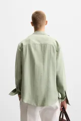 Camisa verde claro de corte relaxed fit confeccionada en tejido con mezcla de modal. Tiene cuello italiano, manga larga con puños abotonados, bolsillo de parche en el pecho y cierre frontal abotonado.
