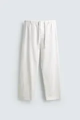Pantalón blanco de corte relajado (relaxed fit) con cintura elástica ajustable mediante cordón y cierre frontal de cremallera y botón. Presenta bolsillos frontales y un bolsillo trasero de vivo con botón.