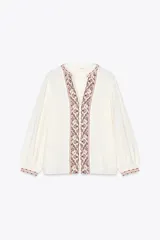 Camisa blanca de cuello redondo con escote en pico y mangas largas abullonadas. Presenta bordados decorativos en el escote, el frente y los puños.
