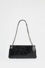 Bolso alargado negro con tachas plateadas en el borde inferior y detalle de cremallera en el corte. Tiene asa de cadena plateada multiposición para usar al hombro o como bandolera. Incluye bolsillo interior con cremallera y cierre principal con cremallera.
