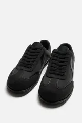 Zapatilla deportiva monocolor negra de cordones, con suela ultrafina y logo lateral.