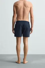 Short de baño celeste de tejido técnico con cintura elástica ajustable con cordón interior y trabillas laterales. Tiene bolsillos frontales y bolsillo trasero con cierre de cremallera. Cuenta con forro interior y cierre frontal con cremallera y botón a presión oculto.