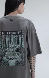Remera de algodón premium color gris oscuro, corte oversize con hombros caídos y cuello redondo. Estampado grande en la espalda con la palabra "KILOMBITO" sobre una ilustración de una figura en un entorno boscoso en tonos verde azulado y negro.
