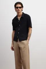 Camisa negra de punto con textura, de corte recto, manga corta, cuello inglés, tapeta lisa, canesú en la espalda y bajo recto con aberturas laterales.