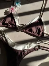 Conjunto de bikini rojo con corpiño triangular con tirantes finos y detalle de aro metálico con forma de corazón en el centro. La bombacha es tipo colaless con tiras finas ajustables en los laterales con detalle de aros metálicos.