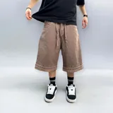 Bermuda de corte baggy color marrón con efecto gastado (lavado vintage), doble carpintero y detalle artesanal visible en el bajo. Incluye un cordón extra confeccionado en la misma tela.