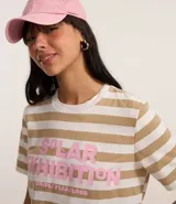 Remera de algodón con poliéster a rayas horizontales color beige y blanco, con cuello redondo y mangas cortas. Estampado frontal con lettering en color rosa.
